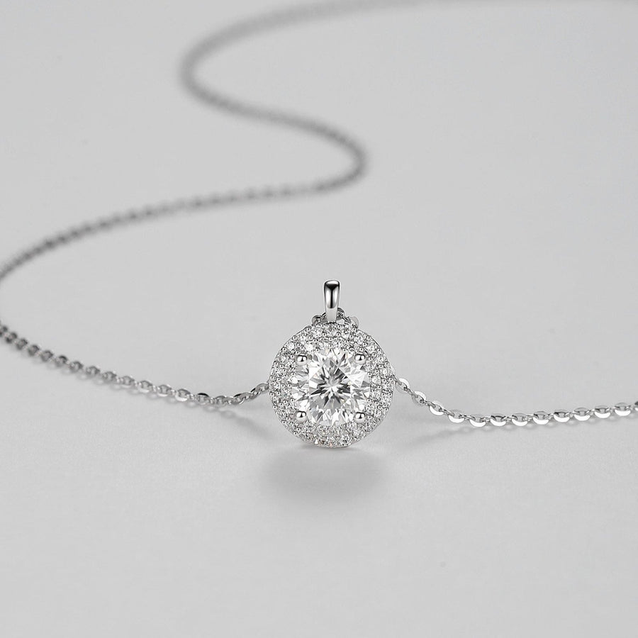 The centerpiece features a 1 carat Moissanite, renowned for its exceptional sparkle and clarity, surrounded by a halo of smaller stones that enhance its radiance. The delicate silver chain complements the pendant perfectly, making it a versatile piece suitable for both everyday wear and special occasions. 