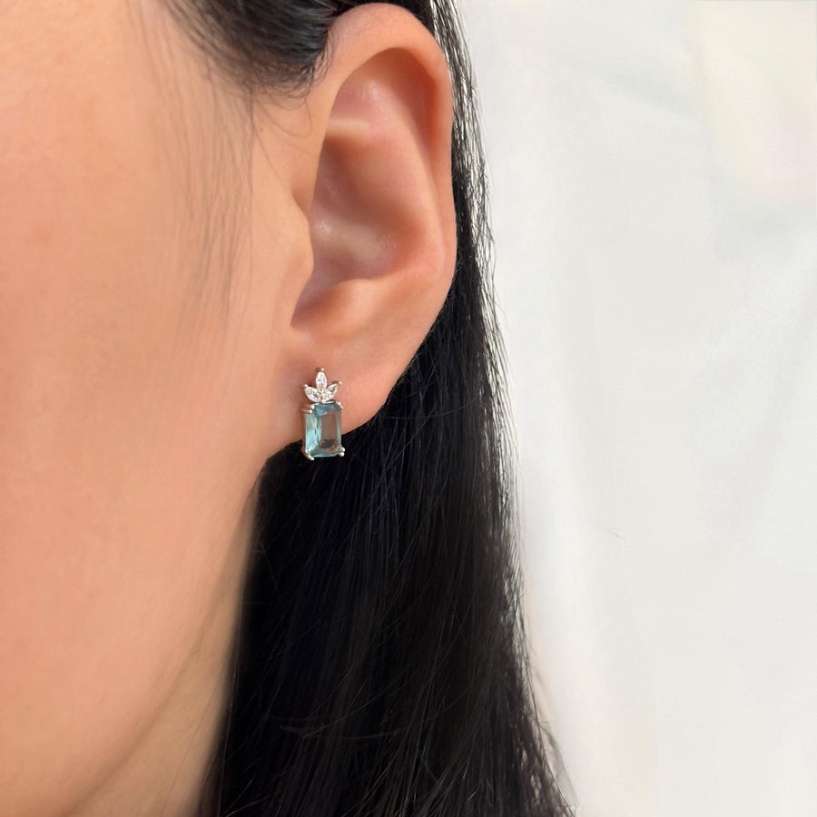 The 925 silver stud earrings feature a captivating emerald-cut aqua blue cubic zircon crowned by a delicate cluster of marquise-cut cubic zircon. Set in a sleek silver finish, these earrings exude refined elegance and fresh sophistication, perfect for both everyday wear and special occasions. 