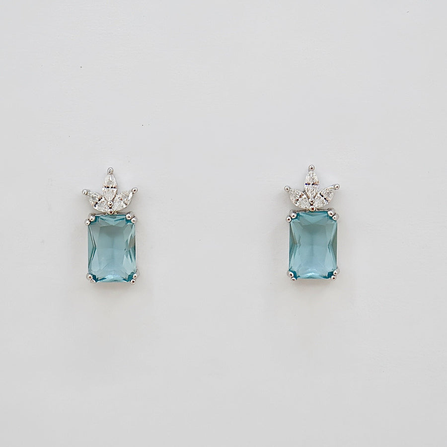 The 925 silver stud earrings feature a captivating emerald-cut aqua blue cubic zircon crowned by a delicate cluster of marquise-cut cubic zircon. Set in a sleek silver finish, these earrings exude refined elegance and fresh sophistication, perfect for both everyday wear and special occasions. 