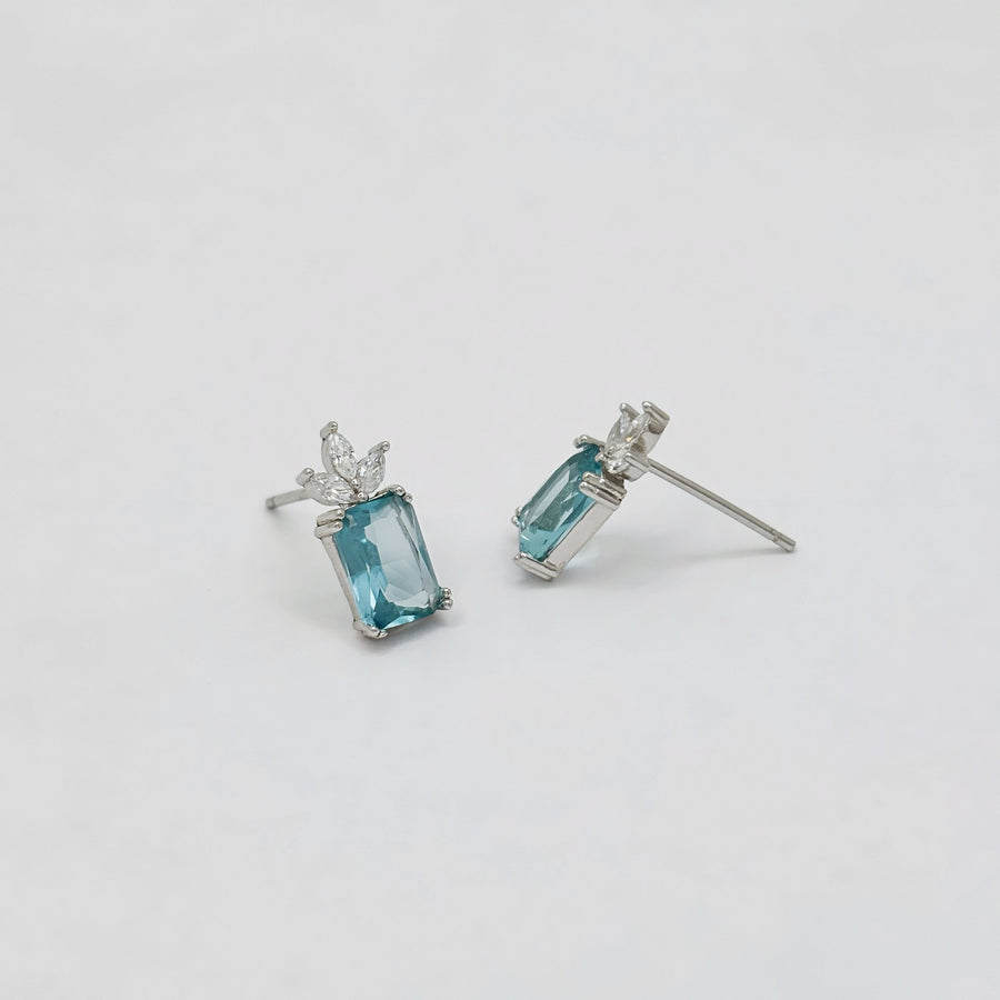 The 925 silver stud earrings feature a captivating emerald-cut aqua blue cubic zircon crowned by a delicate cluster of marquise-cut cubic zircon. Set in a sleek silver finish, these earrings exude refined elegance and fresh sophistication, perfect for both everyday wear and special occasions. 