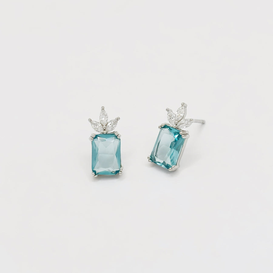 The 925 silver stud earrings feature a captivating emerald-cut aqua blue cubic zircon crowned by a delicate cluster of marquise-cut cubic zircon. Set in a sleek silver finish, these earrings exude refined elegance and fresh sophistication, perfect for both everyday wear and special occasions. 