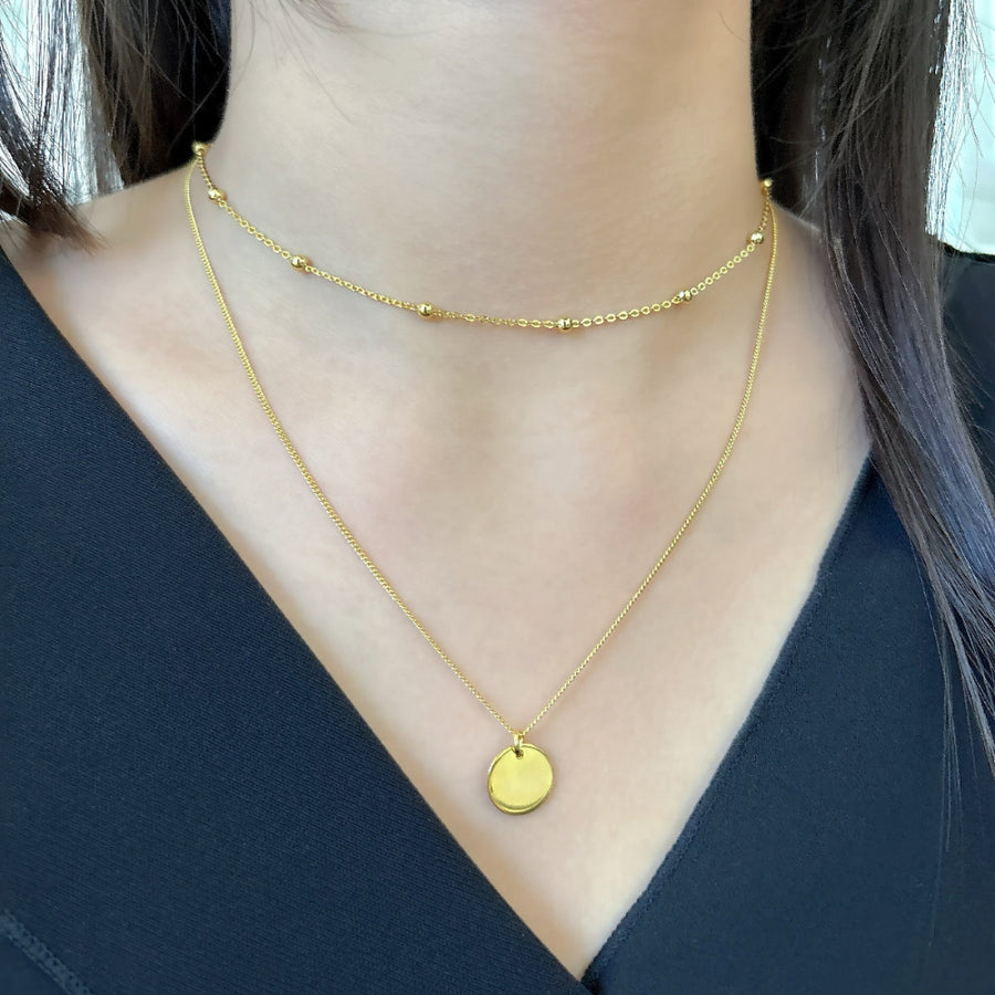 925 Sterling silver necklace. This layered gold necklace combines a sleek coin pendant with delicate bead accents, offering a chic and versatile accessory for any look. Effortlessly elegant, this double-layer design adds depth and charm to your style, perfect for both casual and formal occasions.