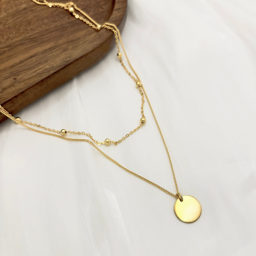 925 Sterling silver necklace. This layered gold necklace combines a sleek coin pendant with delicate bead accents, offering a chic and versatile accessory for any look. Effortlessly elegant, this double-layer design adds depth and charm to your style, perfect for both casual and formal occasions.