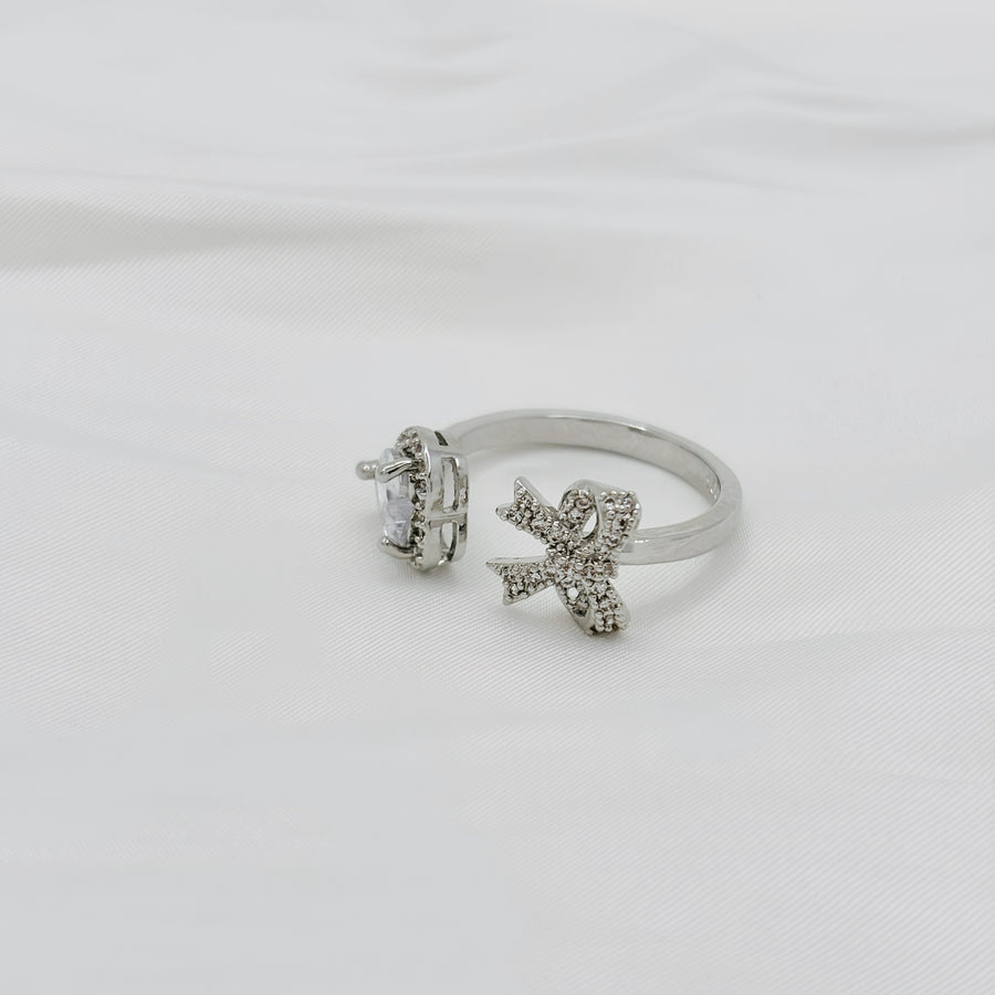 This stunning silver ring features a large, heart shaped gemstone and a decorative bow encrusted with smaller stones, creating a unique and elegant design. 