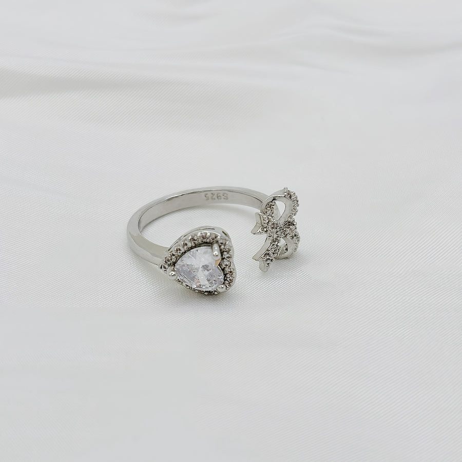 This stunning silver ring features a large, heart shaped gemstone and a decorative bow encrusted with smaller stones, creating a unique and elegant design. 