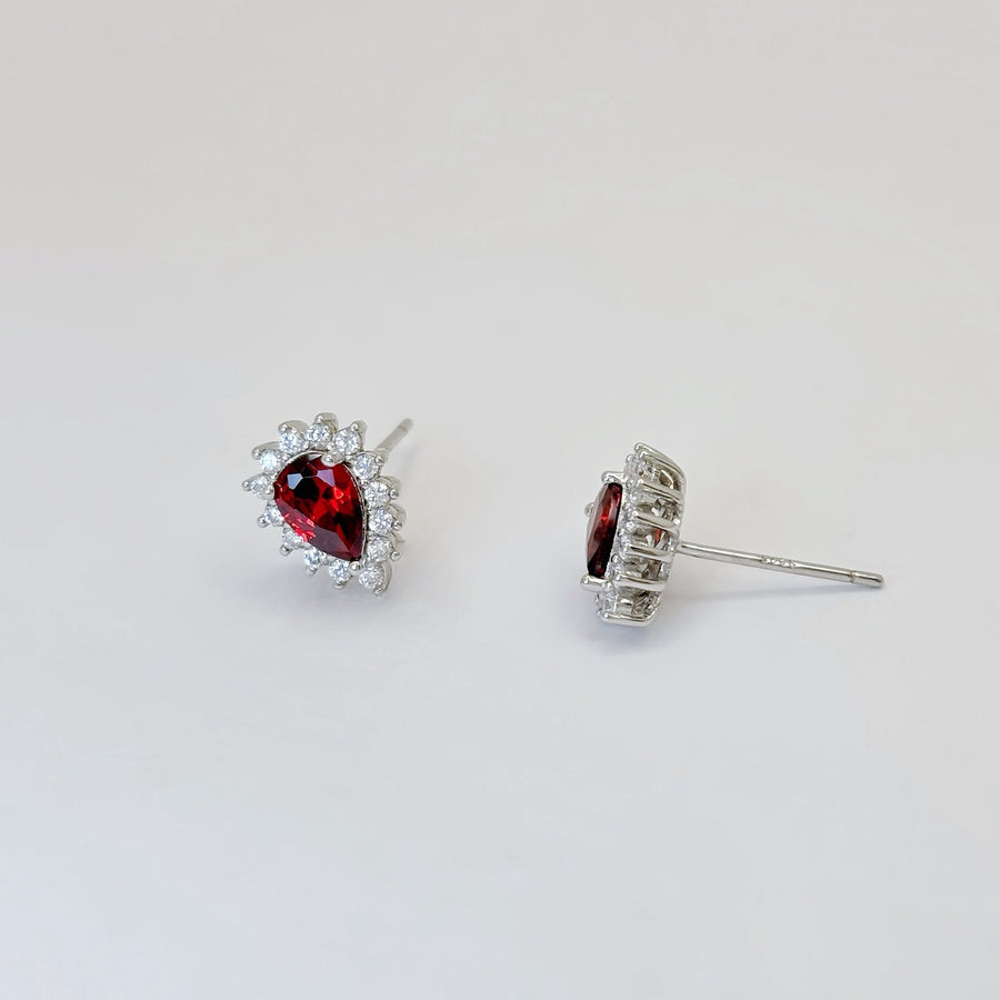 Elevate your elegance with these teardrop-shaped silver stud earrings, showcasing a stunning red cubic zircon encircled by dazzling cubic zircon accents. A timeless design that adds a touch of glamour to any outfit.