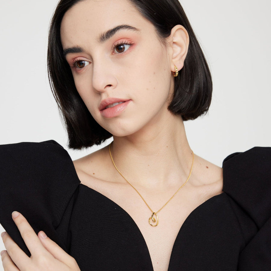 This elegant silver necklace features a delicate gold chain and a unique, abstract heart-shaped pendant. The pendant's fluid, organic design adds a modern twist to a classic symbol of love, making it a perfect accessory for any occasion. 