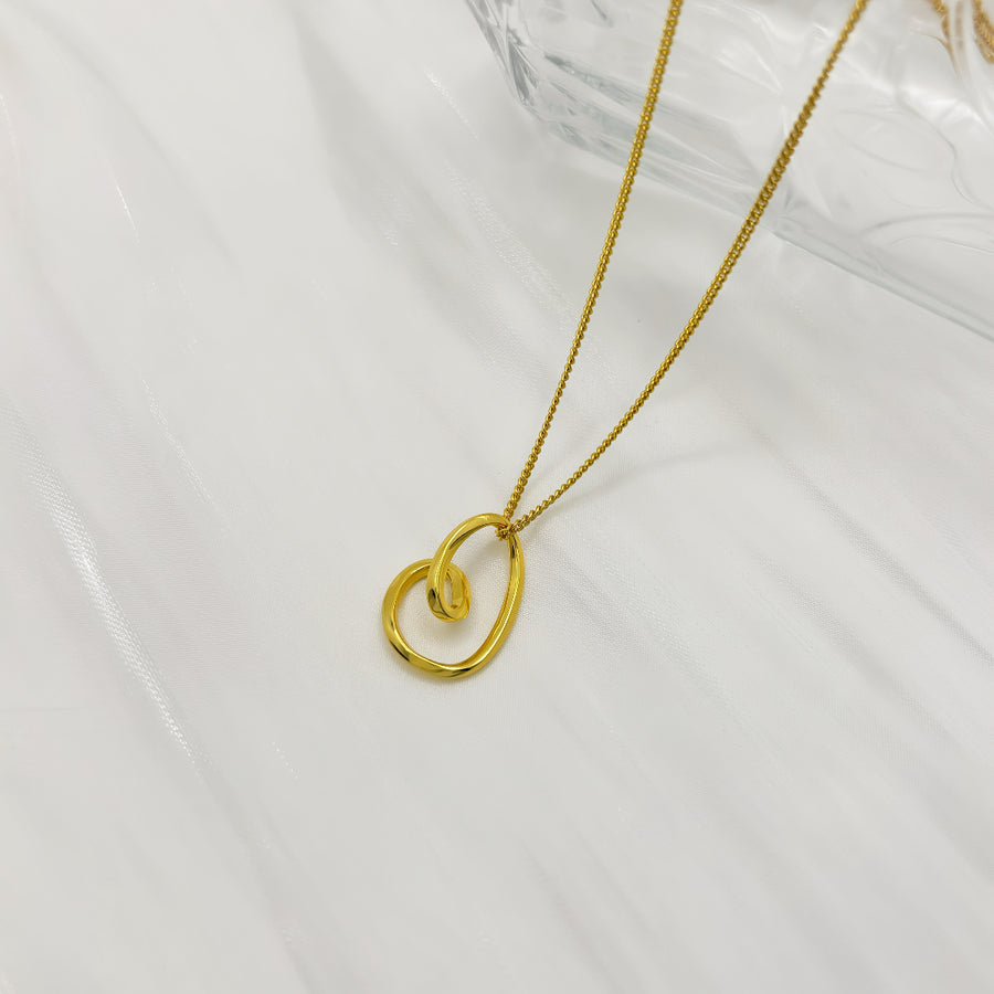 This elegant silver necklace features a delicate gold chain and a unique, abstract heart-shaped pendant. The pendant's fluid, organic design adds a modern twist to a classic symbol of love, making it a perfect accessory for any occasion. 