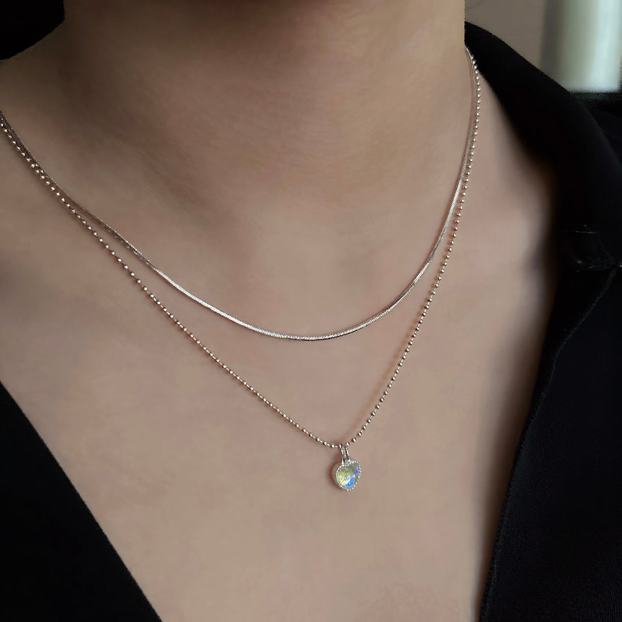 This silver necklace features a stunning moonstone heart-shaped pendant, radiating both beauty and kindness. Its unique design combines beaded and snake chain elements, creating a dual-layered chain for a visually striking effect that exudes a sense of fluidity.