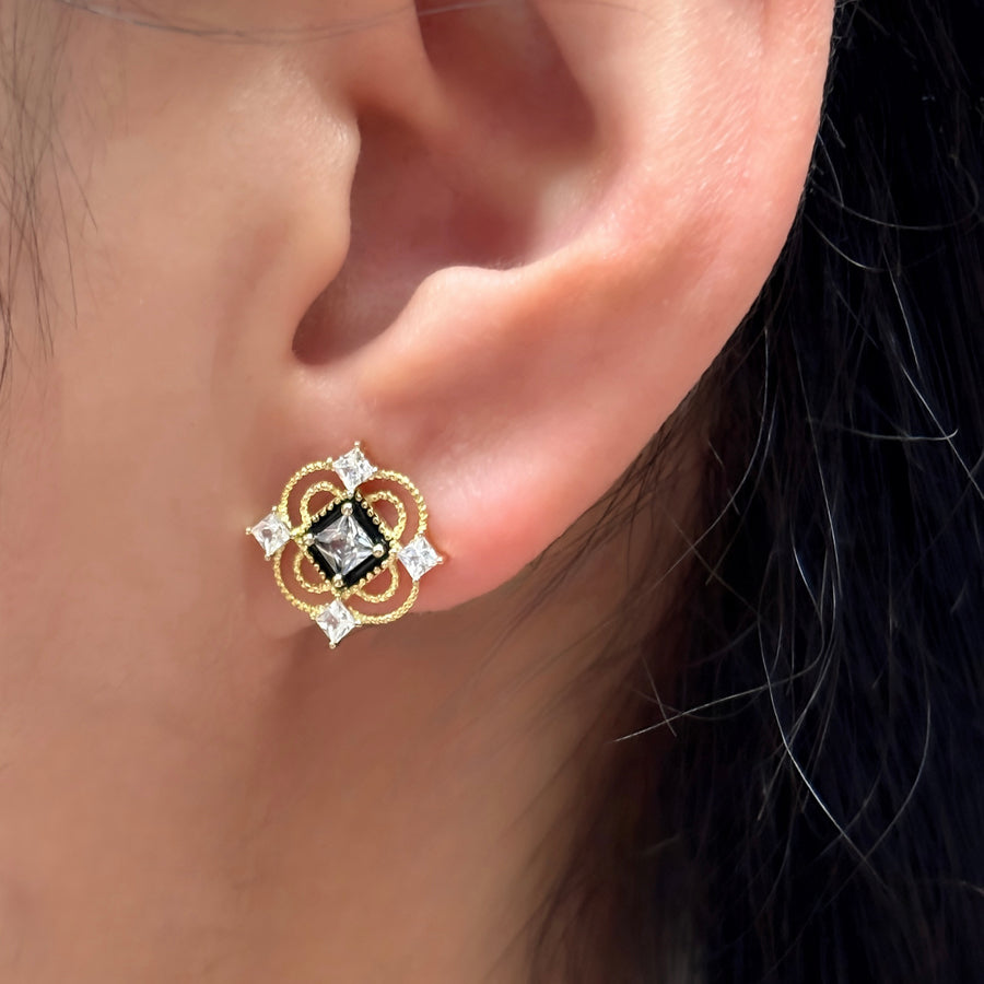 These vintage-inspired silver stud earrings feature a striking black square framed by intricate gold details and shimmering cubic zirconia accents. Perfect for adding a touch of glamour and sophistication to any outfit. 