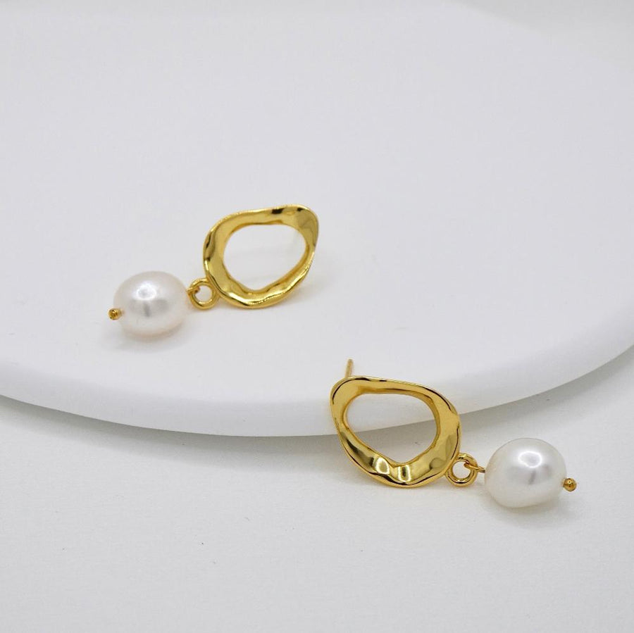 These elegant silver earrings feature a unique, irregularly shaped gold frame that adds a touch of modern sophistication. Suspended from each frame is a lustrous, white pearl, creating a timeless and classic look perfect for any occasion. The combination of the unconventional gold frame and the classic pearl makes these earrings a versatile accessory that enhances both contemporary and traditional styles.