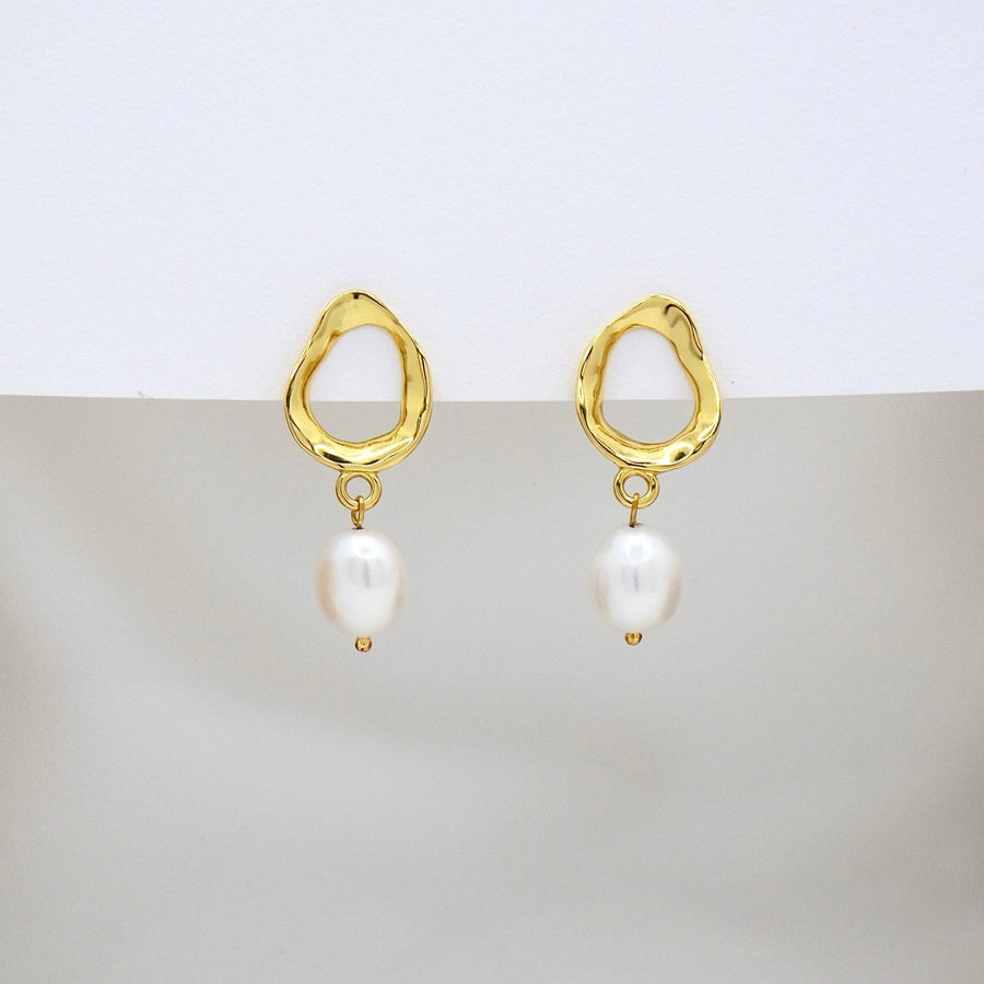 These elegant silver earrings feature a unique, irregularly shaped gold frame that adds a touch of modern sophistication. Suspended from each frame is a lustrous, white pearl, creating a timeless and classic look perfect for any occasion. The combination of the unconventional gold frame and the classic pearl makes these earrings a versatile accessory that enhances both contemporary and traditional styles.