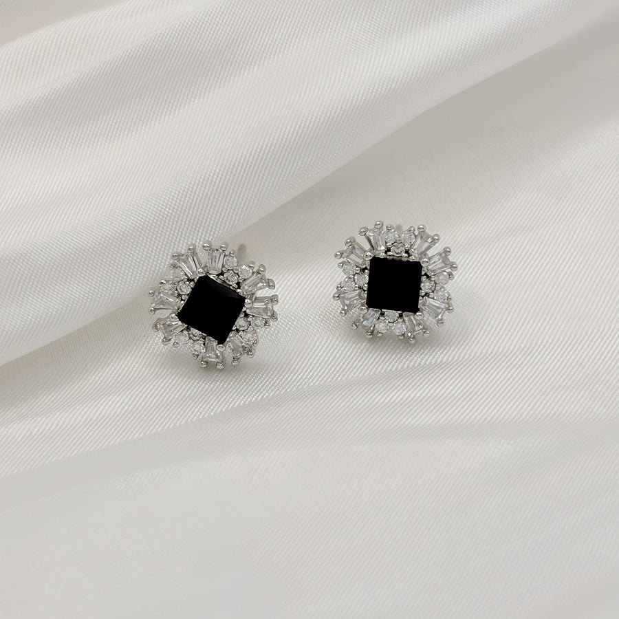 These stunning black cubic zirconia silver stud earrings are surrounded by a burst of shimmering cubic zirconia, creating a striking starburst design.