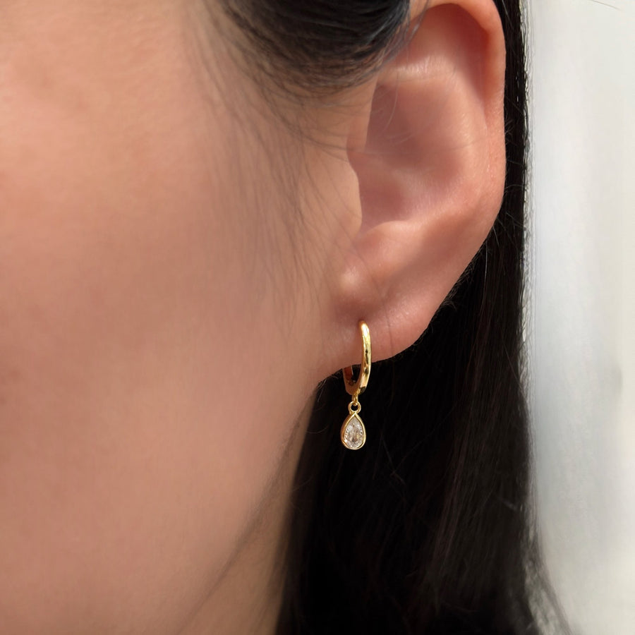 These elegant gold hoop earrings feature a delicate teardrop-shaped cubic zircon pendant, adding a touch of sophistication and sparkle to any outfit. Perfect for both casual and formal occasions, these earrings are a timeless addition to any jewelry collection.