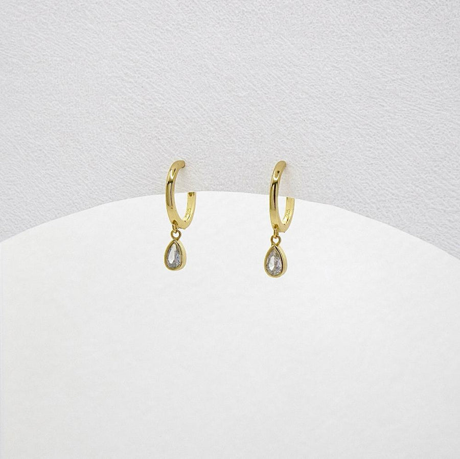 These elegant gold hoop earrings feature a delicate teardrop-shaped cubic zircon pendant, adding a touch of sophistication and sparkle to any outfit. Perfect for both casual and formal occasions, these earrings are a timeless addition to any jewelry collection.