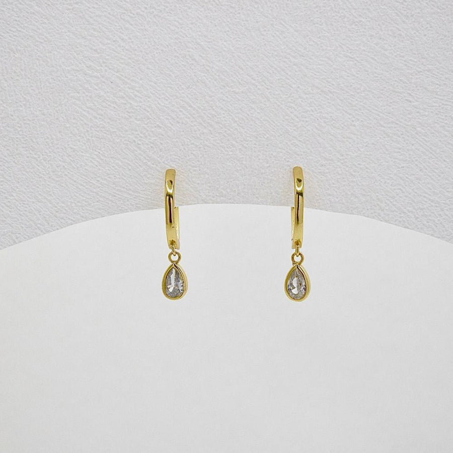 These elegant gold hoop earrings feature a delicate teardrop-shaped cubic zircon pendant, adding a touch of sophistication and sparkle to any outfit. Perfect for both casual and formal occasions, these earrings are a timeless addition to any jewelry collection.