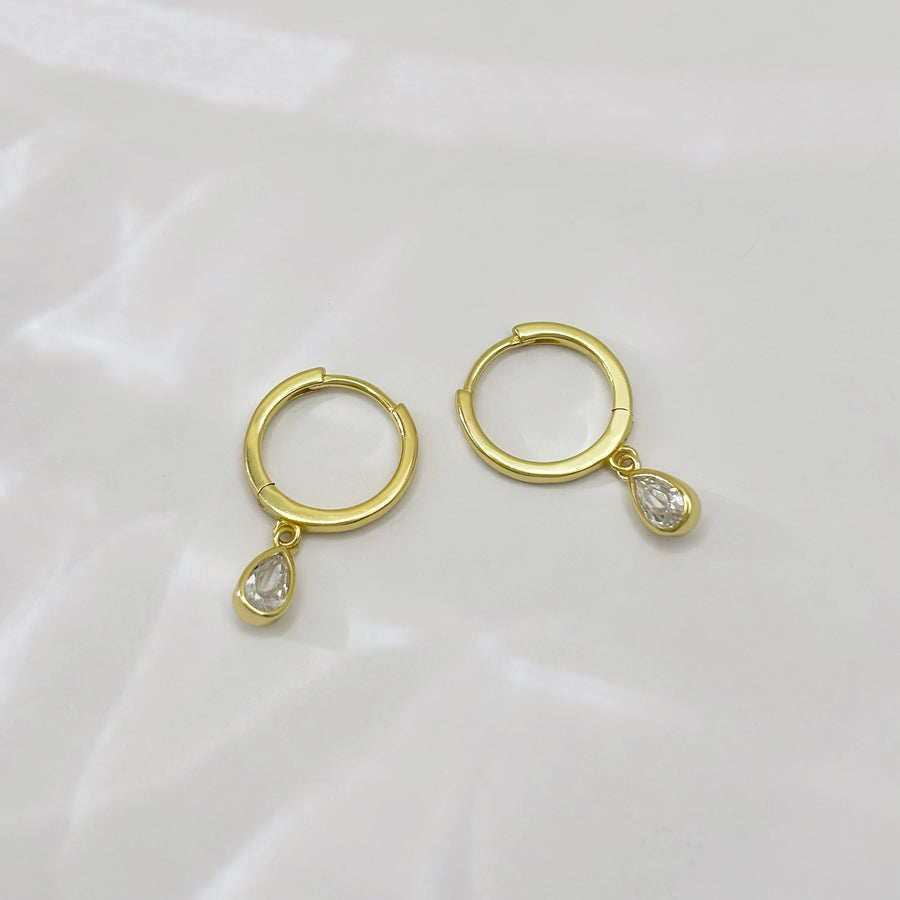 These elegant gold hoop earrings feature a delicate teardrop-shaped cubic zircon pendant, adding a touch of sophistication and sparkle to any outfit. Perfect for both casual and formal occasions, these earrings are a timeless addition to any jewelry collection.