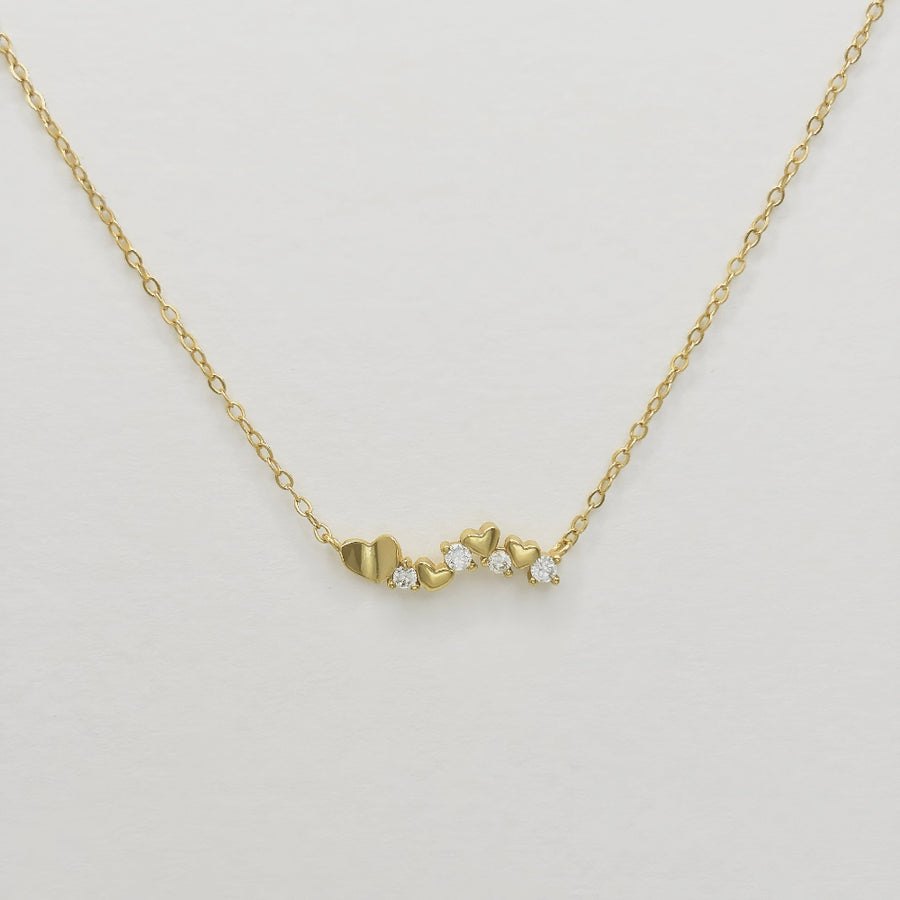 This elegant necklace features a delicate gold chain adorned with a series of small gold hearts interspersed with sparkling cubic zircon. The design is both charming and sophisticated, making it a perfect accessory for any occasion. 