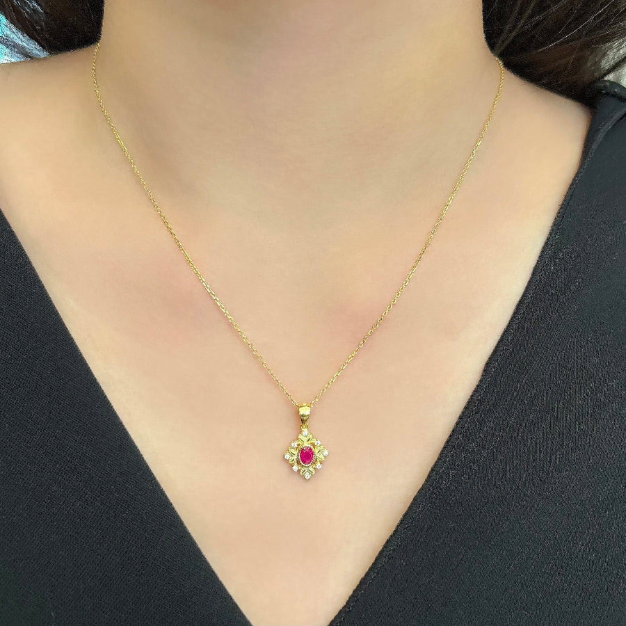 This delicate gold necklace features an intricately designed pendant with a central red cubic zircon, surrounded by a floral pattern and small clear cubic zircon. The elegant design adds a touch of sophistication and charm to any outfit. Perfect for special occasions or everyday wear, this necklace adds a touch of timeless sophistication to any outfit with its brilliant sparkle.