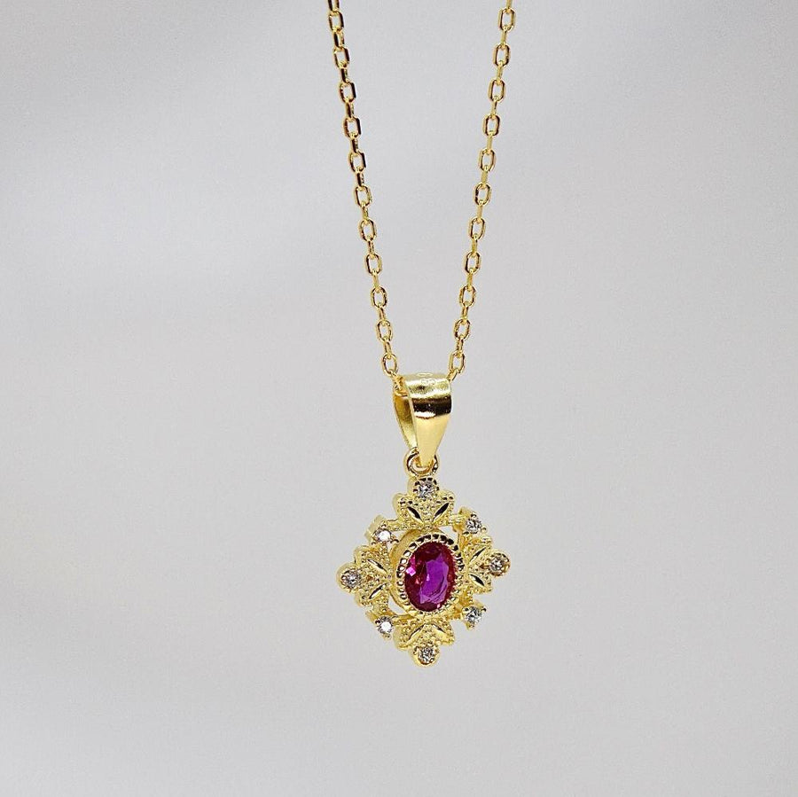 This delicate gold necklace features an intricately designed pendant with a central red cubic zircon, surrounded by a floral pattern and small clear cubic zircon. The elegant design adds a touch of sophistication and charm to any outfit. Perfect for special occasions or everyday wear, this necklace adds a touch of timeless sophistication to any outfit with its brilliant sparkle.