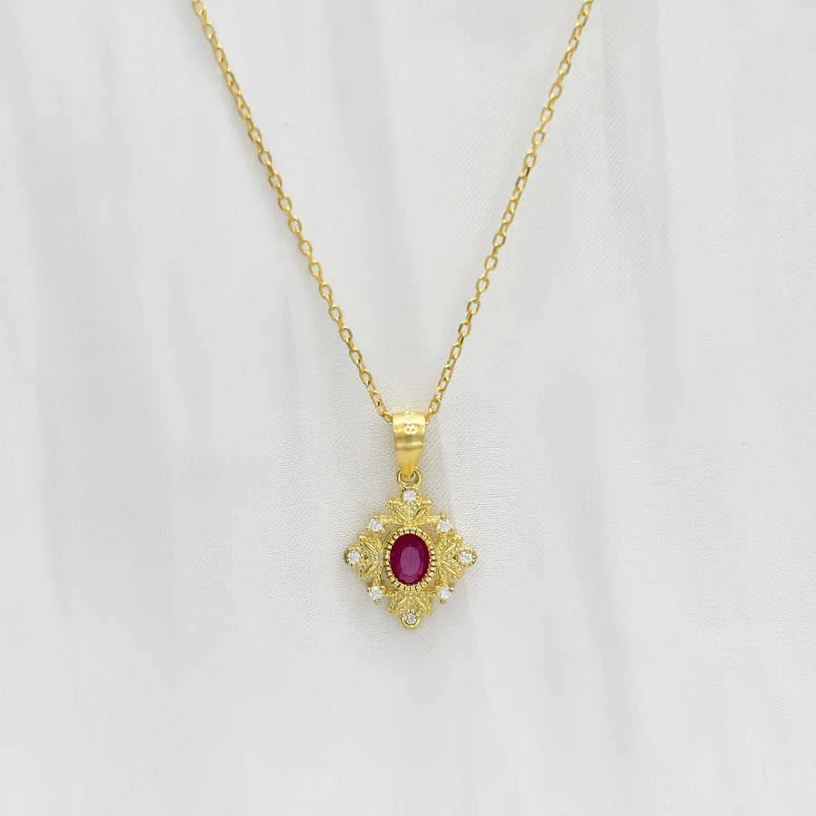 This delicate gold necklace features an intricately designed pendant with a central red cubic zircon, surrounded by a floral pattern and small clear cubic zircon. The elegant design adds a touch of sophistication and charm to any outfit. Perfect for special occasions or everyday wear, this necklace adds a touch of timeless sophistication to any outfit with its brilliant sparkle.