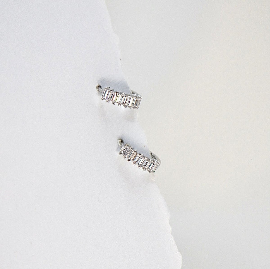 These stunning hoop earrings feature a row of baguette-cut cubic zircon, adding a touch of sophistication to any outfit. Crafted from high-quality materials, these earrings are perfect for both everyday wear and special occasions. 