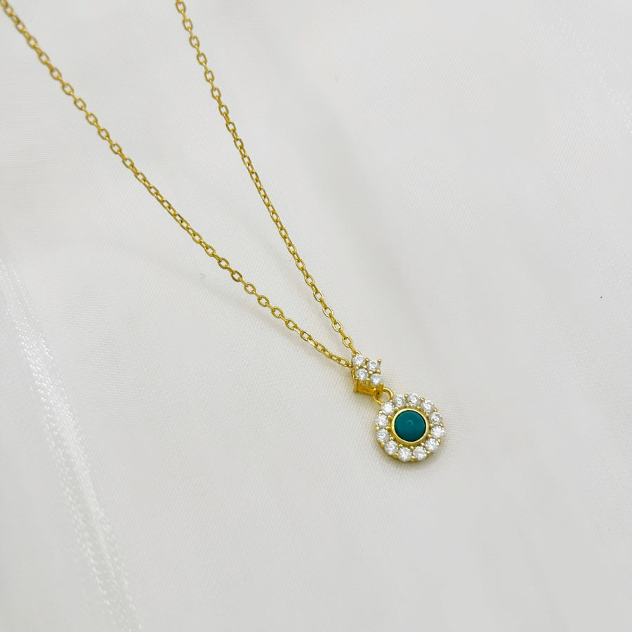 This elegant necklace features a delicate gold chain and a pendant adorned with a central turquoise stone, surrounded by a halo of sparkling cubic zircon. The combination of the vibrant turquoise and the shimmering cubic zircon creates a striking and timeless piece of jewelry. Perfect for any occasion, this necklace adds a touch of sophistication and color to your look, making it a versatile addition to any jewelry collection.