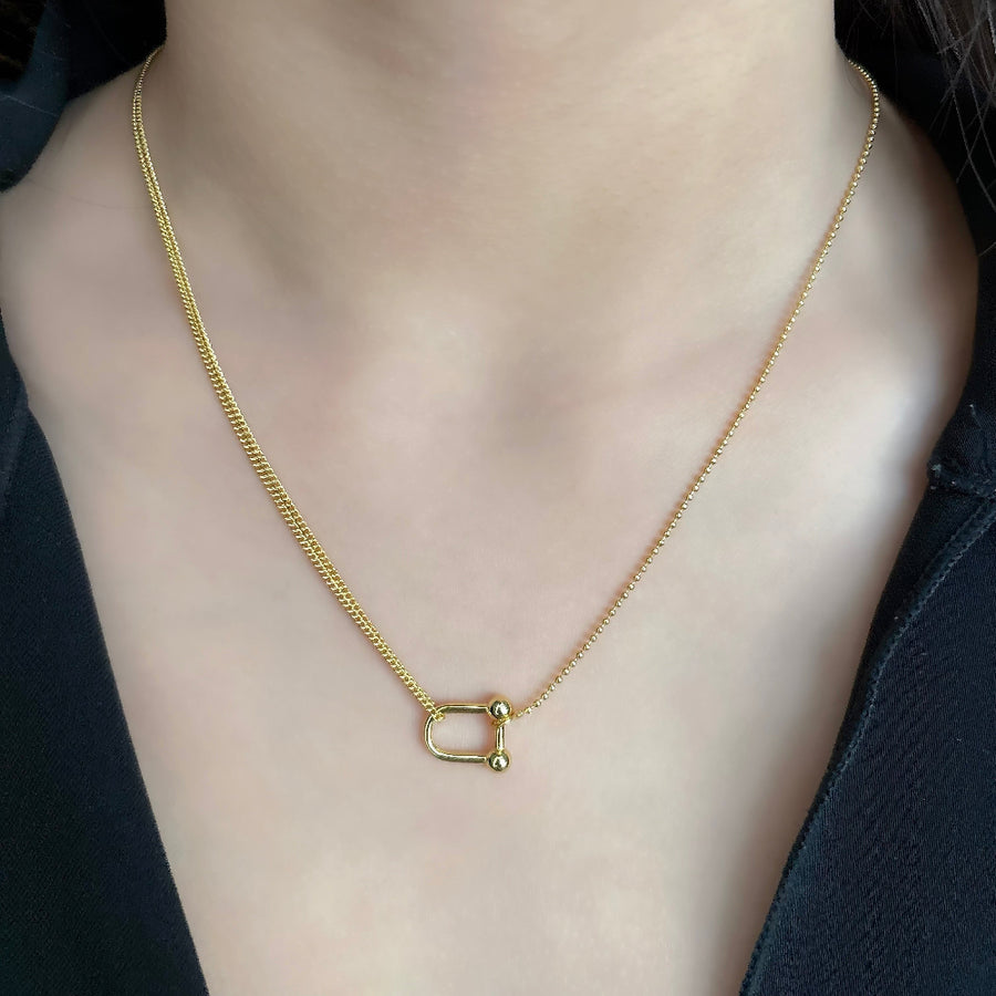 This elegant necklace features a unique design with two different types of chains: a delicate beaded chain and a cable chain. The centerpiece is a gold-toned U-shaped clasp that connects the two chains, adding a modern and stylish touch to the piece. Perfect for both casual and formal occasions, this necklace effortlessly combines contemporary style with classic elegance.