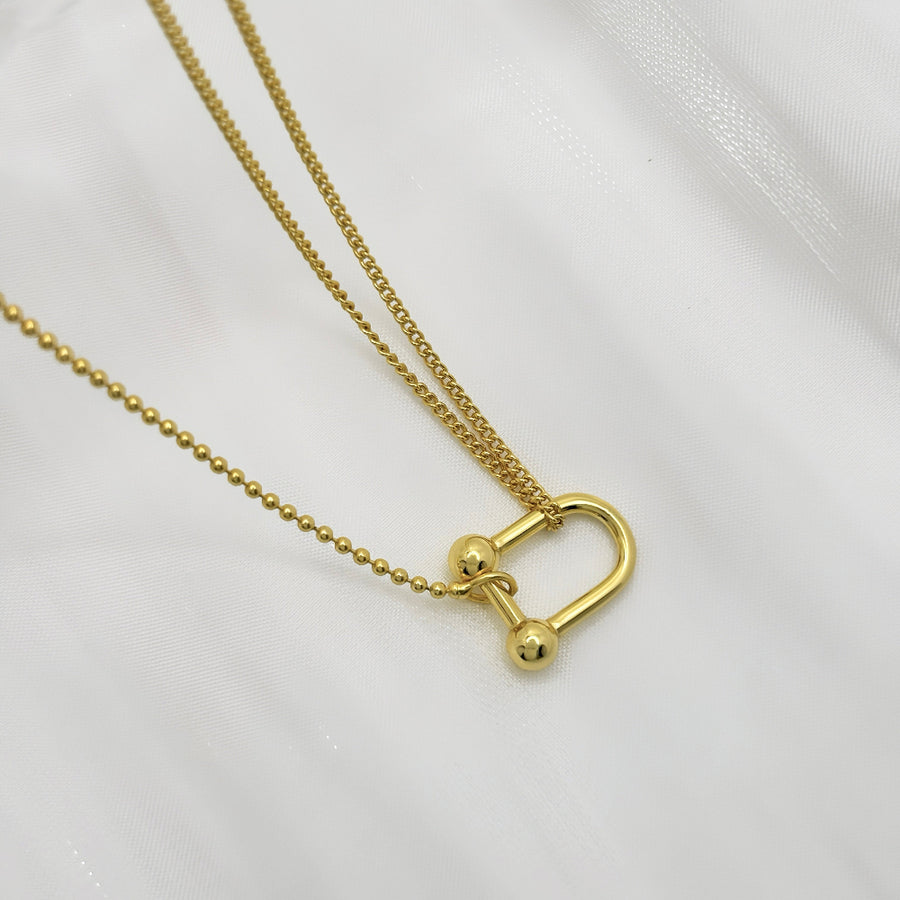 This elegant necklace features a unique design with two different types of chains: a delicate beaded chain and a cable chain. The centerpiece is a gold-toned U-shaped clasp that connects the two chains, adding a modern and stylish touch to the piece. Perfect for both casual and formal occasions, this necklace effortlessly combines contemporary style with classic elegance.