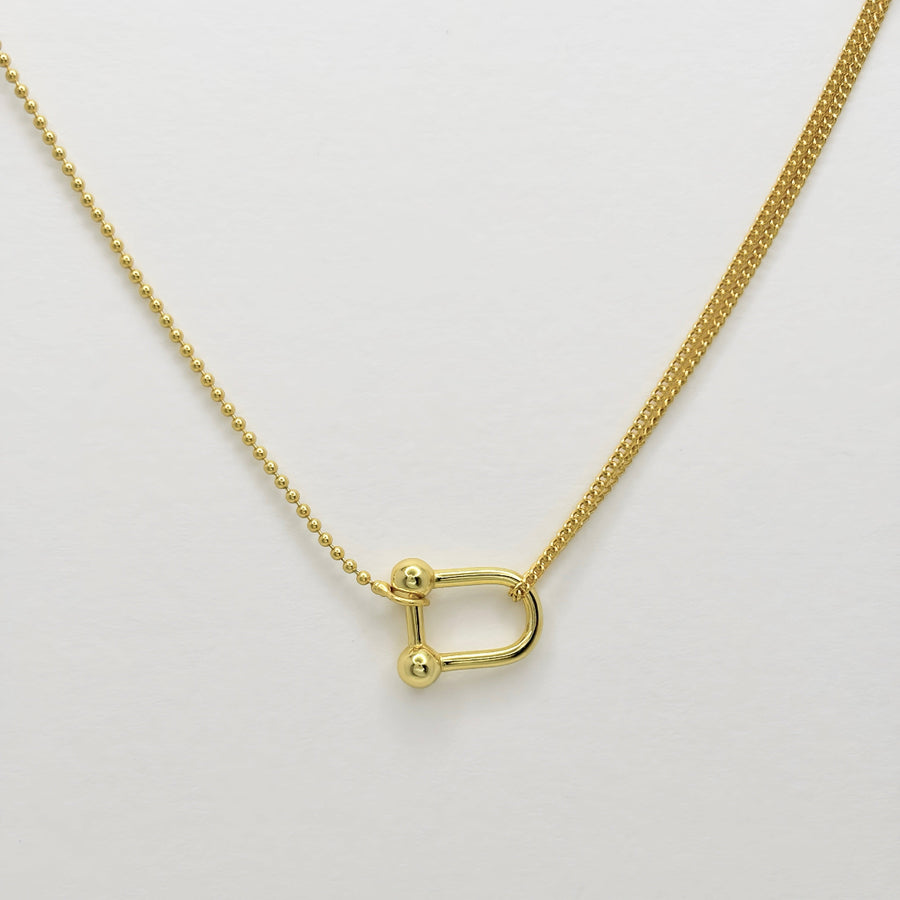 This elegant necklace features a unique design with two different types of chains: a delicate beaded chain and a cable chain. The centerpiece is a gold-toned U-shaped clasp that connects the two chains, adding a modern and stylish touch to the piece. Perfect for both casual and formal occasions, this necklace effortlessly combines contemporary style with classic elegance.