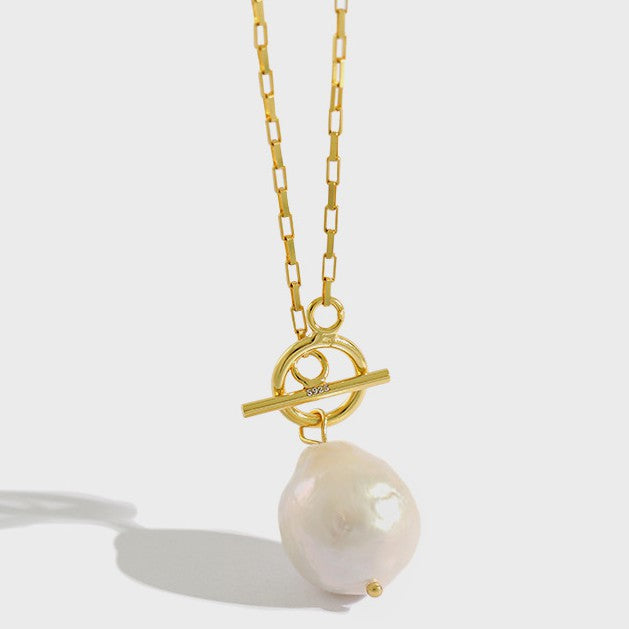 This necklace features a large, irregularly shaped baroque pearl pendant suspended from a gold chain. The chain has a toggle clasp with a circular ring and a horizontal bar, adding a stylish and functional element to the design. Perfect for both special occasions and everyday wear, this necklace combines the natural beauty of baroque pearls with contemporary elegance.